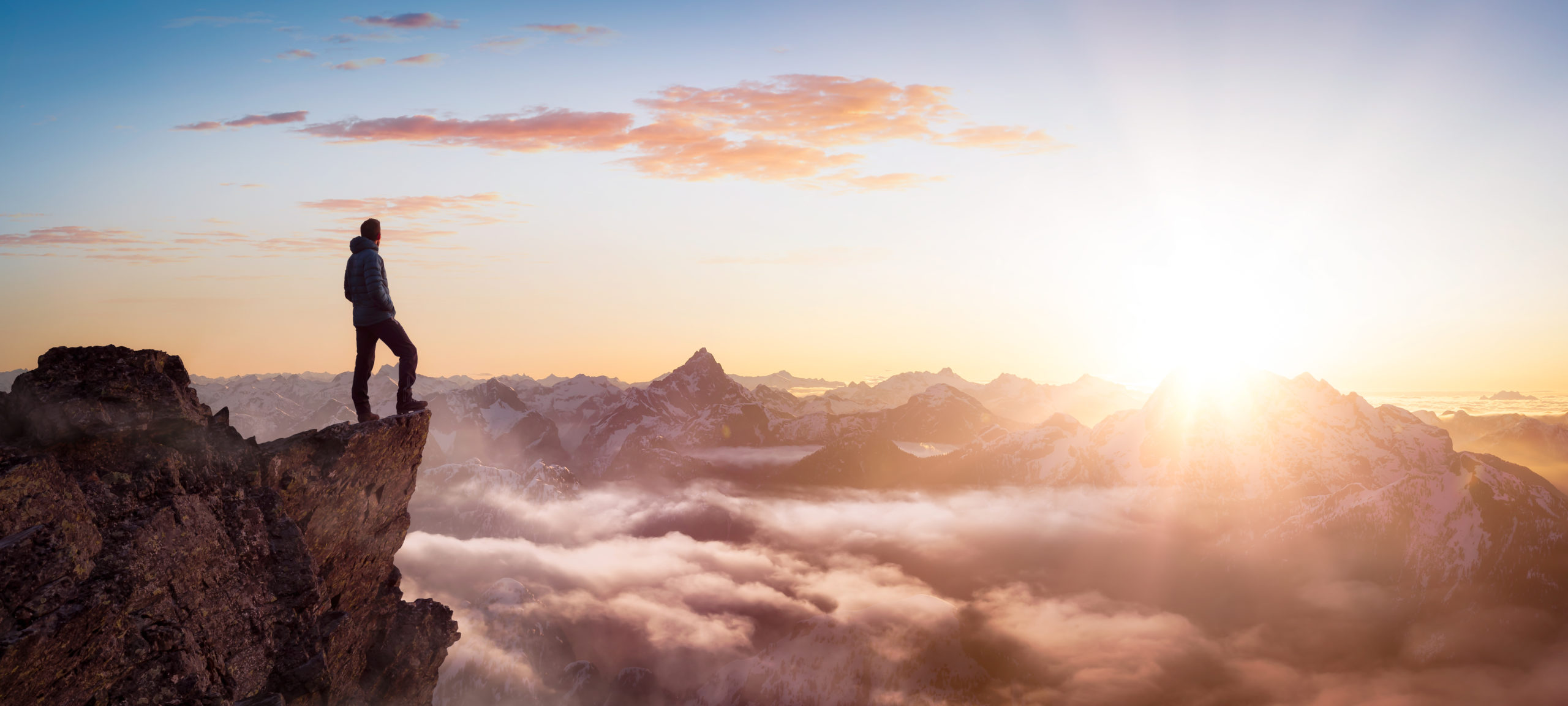 A person standing at the top of a mountain looking at the landscape and the sun