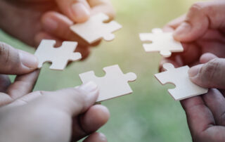 People holding puzzle pieces together for teamwork.