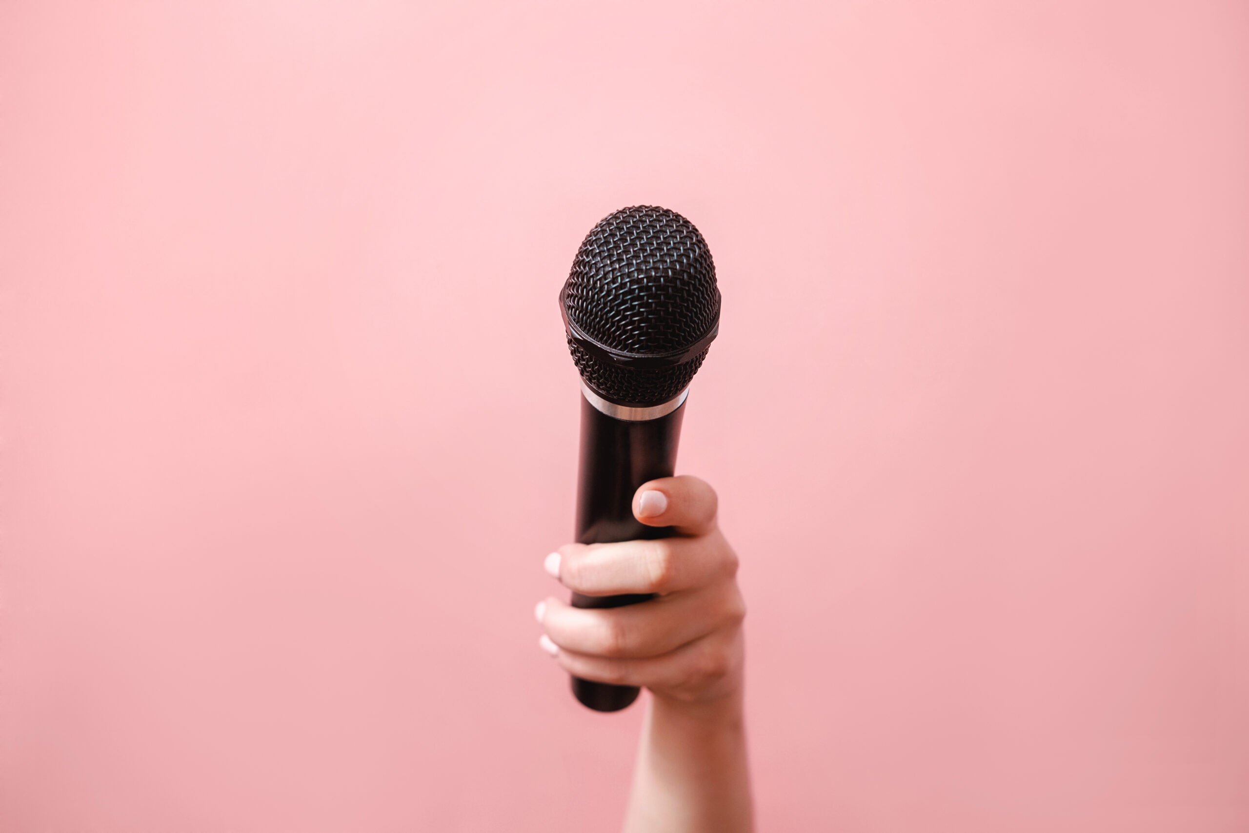 Female hand holding a microphone on a pink background