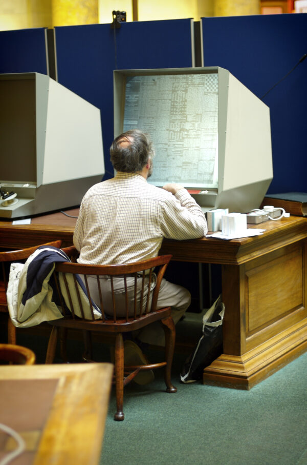 Man sitting at a desk looking at an old microfilm reader