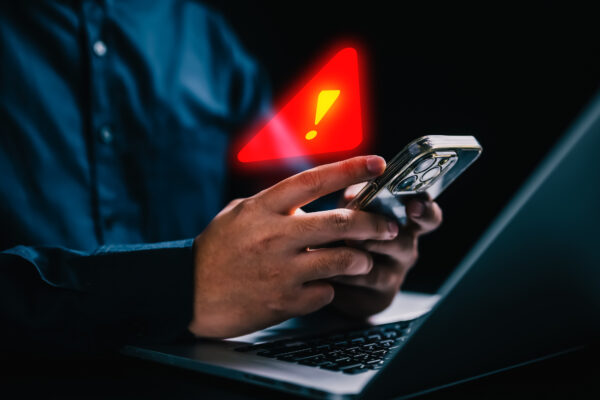 Man looking at laptop and phone, seeing a red warning sign