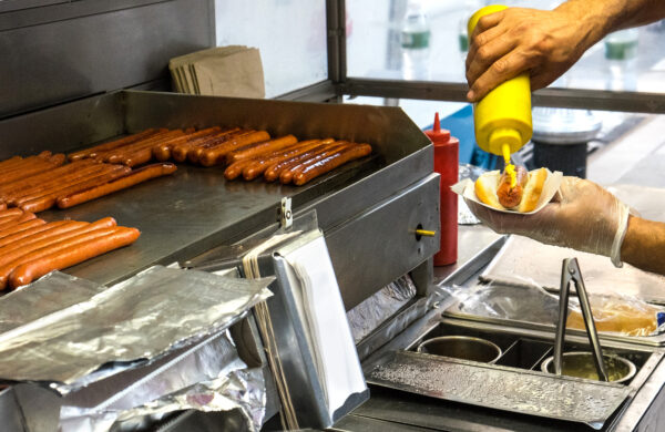 Hot dog vendor making a hot dog with mustard