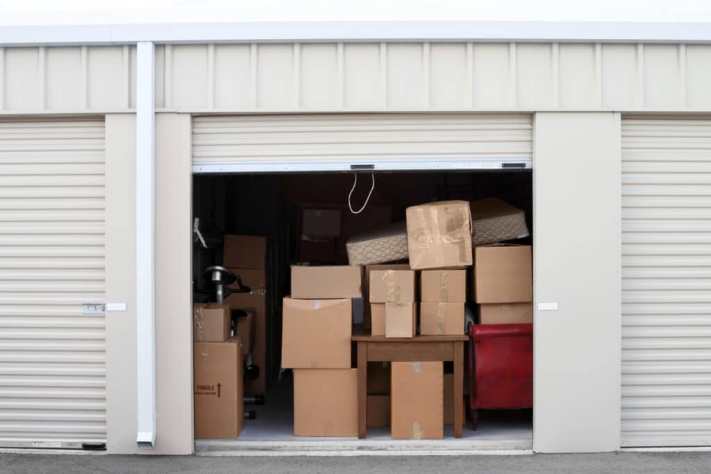 Self storage warehouse building with an open unit. Warehouse building with self storage units. Self storage facility. Roll up doors on self storage facility. One door open with boxes and furniture in doorway.