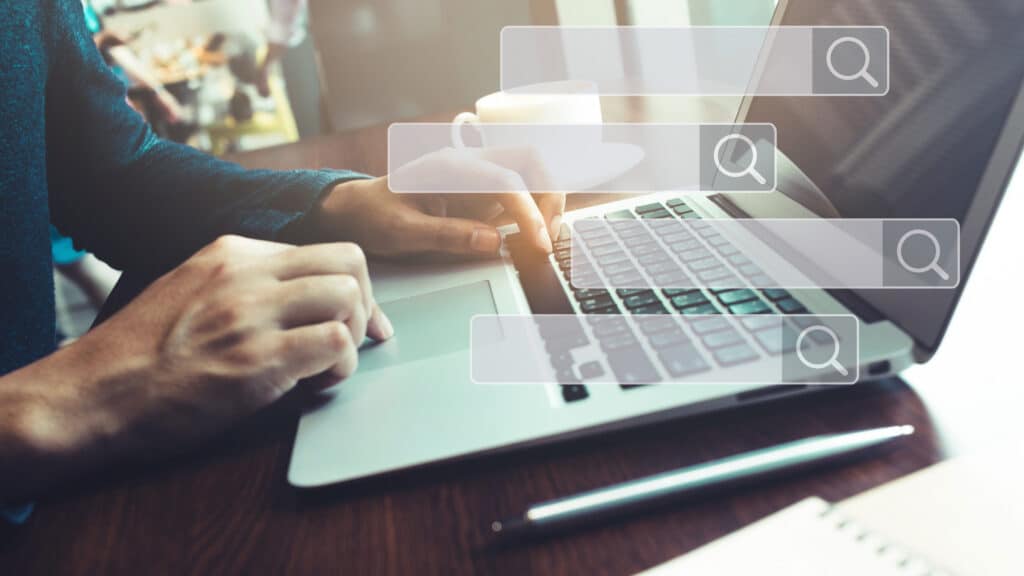 Searching and big data concepts with male hand using computer laptop in cafe bar with search engine icon sign.