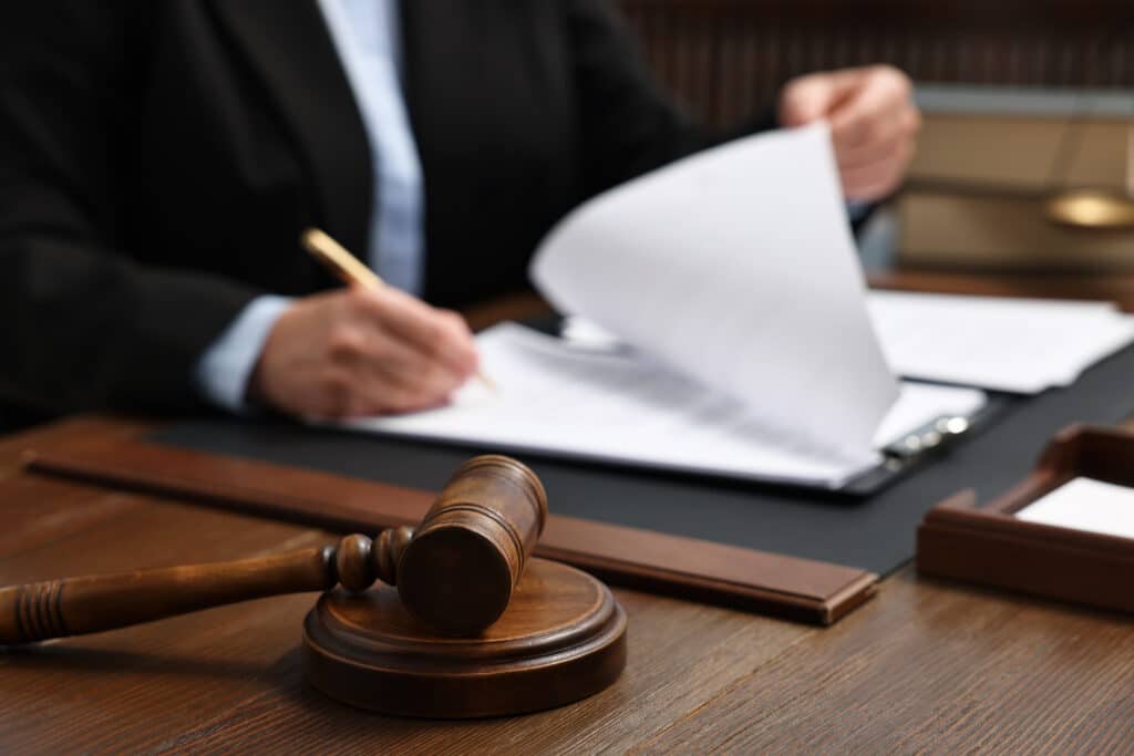 Lawyer working with documents at wooden table indoors, focus on gavel Lawyer working with documents at wooden table indoors, focus on gavel