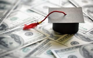 Graduation mortar board cap on one hundred dollar bills concept for the cost of a college and university education