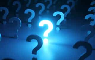 Bright, glowing question mark standing out in a crowd of dark question marks, representing a brilliant idea, solution, or answer to a problem in a conceptual blue illuminated environment