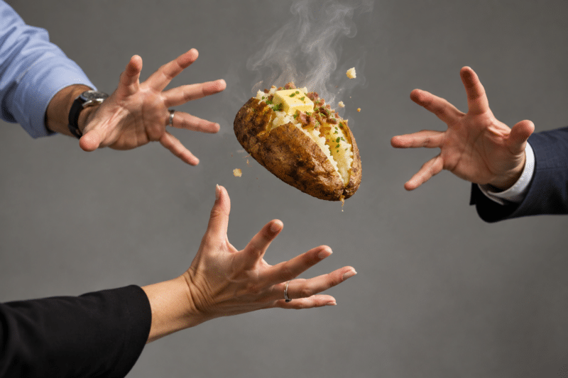 A steaming hot potato caught mid-air between three sets of outstretched hands